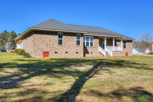 back of house with crawl space, a garage, brick siding, and a yard