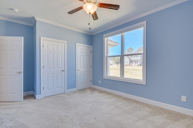 unfurnished bedroom featuring multiple closets, ornamental molding, carpet flooring, ceiling fan, and baseboards