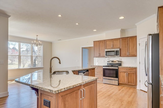 kitchen with backsplash, appliances with stainless steel finishes, light wood-style floors, brown cabinetry, and a sink