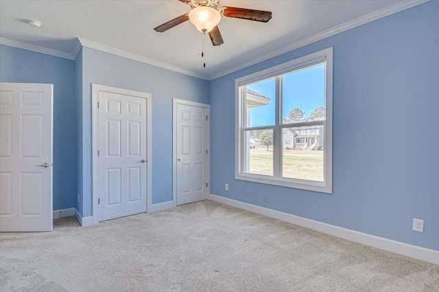 unfurnished bedroom with baseboards, carpet floors, ceiling fan, multiple closets, and crown molding