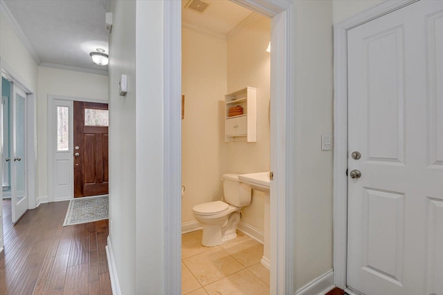 half bathroom with toilet, wood finished floors, visible vents, baseboards, and crown molding