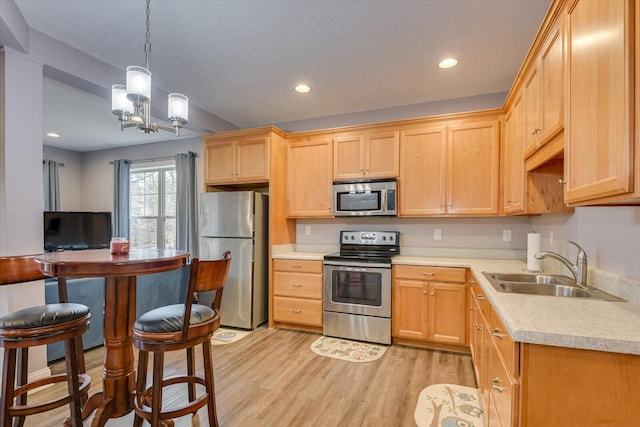 kitchen featuring stainless steel appliances, a sink, hanging light fixtures, light countertops, and light wood-type flooring