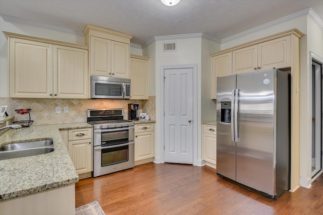 kitchen with visible vents, light stone countertops, stainless steel appliances, light wood-style floors, and a sink