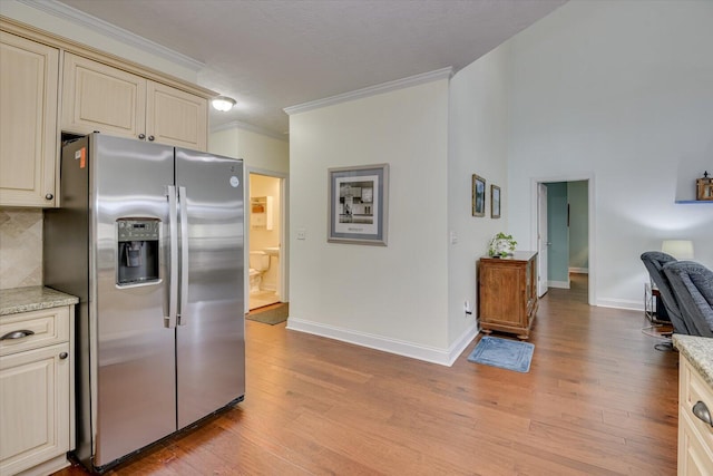 kitchen featuring light wood finished floors, stainless steel fridge, light stone counters, ornamental molding, and cream cabinets