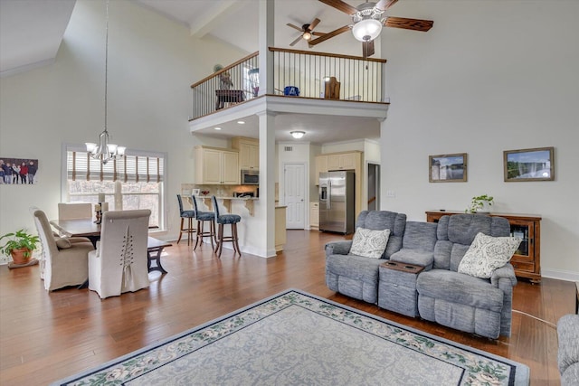 living room featuring baseboards, dark wood finished floors, beamed ceiling, and ceiling fan with notable chandelier