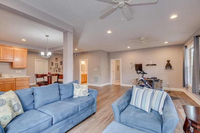 living room featuring light wood finished floors, recessed lighting, visible vents, baseboards, and ceiling fan with notable chandelier