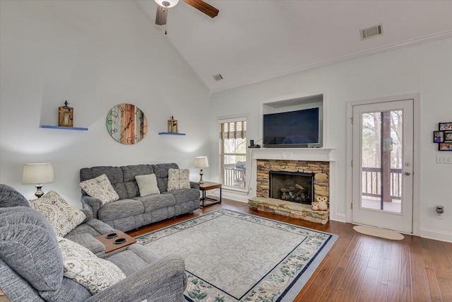 living area featuring dark wood-style floors, visible vents, high vaulted ceiling, and a stone fireplace