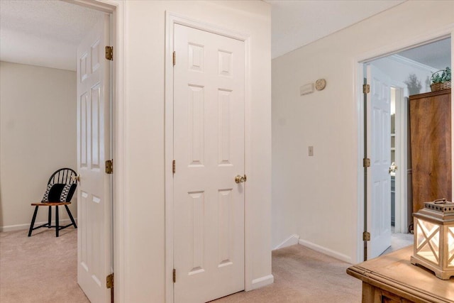 hall featuring light colored carpet and baseboards