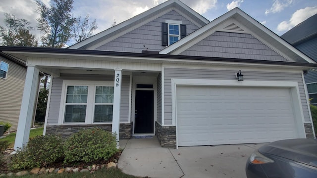 view of front of home featuring a porch, driveway, a garage, and stone siding