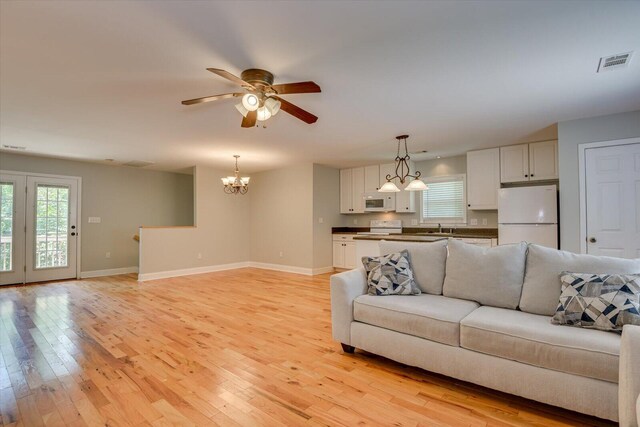 living room featuring light wood-type flooring, ceiling fan with notable chandelier, and sink