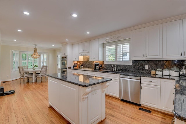 kitchen featuring stainless steel dishwasher, dark stone counters, sink, white cabinets, and hanging light fixtures