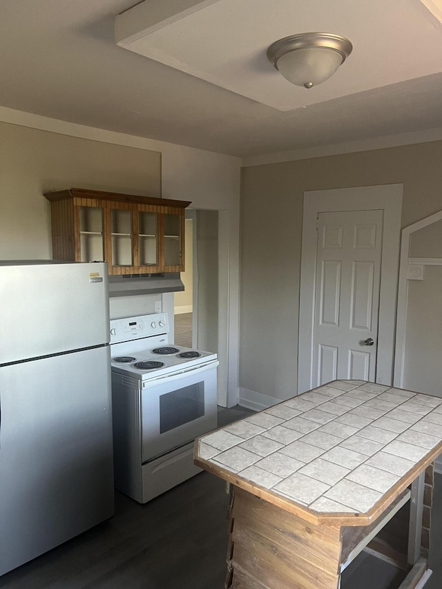 kitchen with tile countertops, range hood, white electric range, and stainless steel refrigerator