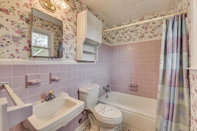 bathroom with a wainscoted wall, a sink, and wallpapered walls