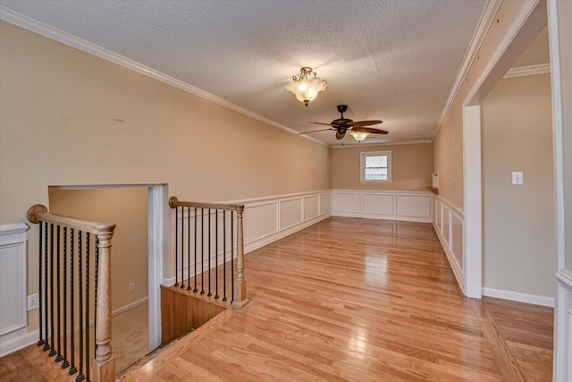 empty room featuring light wood-style floors, a textured ceiling, a decorative wall, and crown molding