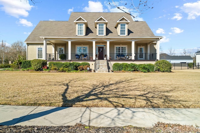 new england style home featuring a porch, a front lawn, a shingled roof, and stucco siding