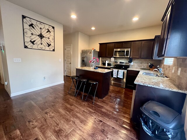 kitchen with sink, dark wood-type flooring, a breakfast bar, a kitchen island, and appliances with stainless steel finishes