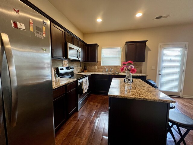 kitchen featuring light stone countertops, appliances with stainless steel finishes, dark hardwood / wood-style flooring, sink, and a kitchen island