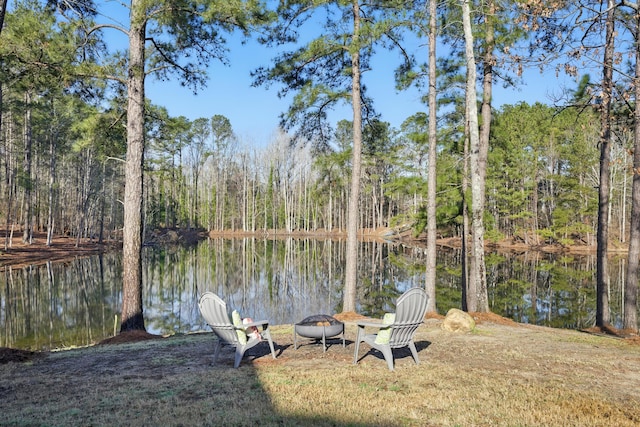 exterior space featuring a forest view, a water view, and an outdoor fire pit