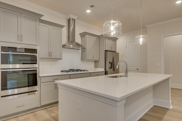 kitchen featuring appliances with stainless steel finishes, light stone counters, wall chimney exhaust hood, gray cabinetry, and a kitchen island with sink