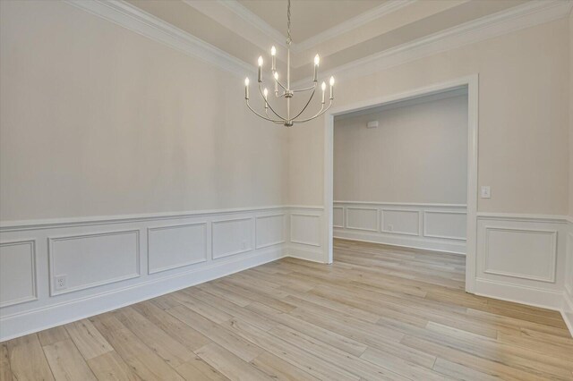 spare room with a notable chandelier, ornamental molding, and light hardwood / wood-style flooring