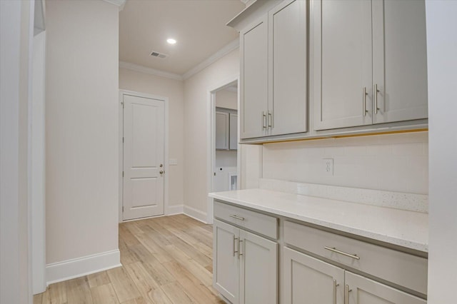 kitchen featuring gray cabinetry, tasteful backsplash, light stone counters, crown molding, and light hardwood / wood-style floors