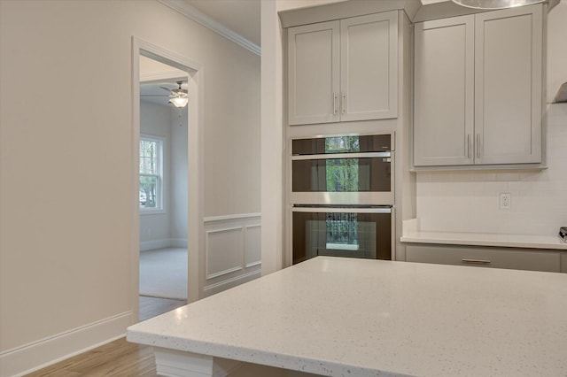 kitchen featuring light stone countertops, double oven, crown molding, ceiling fan, and gray cabinets