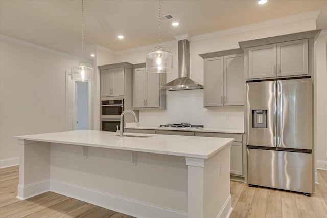 kitchen with wall chimney exhaust hood, stainless steel appliances, sink, a center island with sink, and gray cabinets