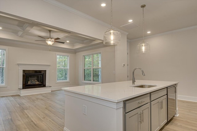 kitchen featuring coffered ceiling, hanging light fixtures, sink, an island with sink, and beamed ceiling