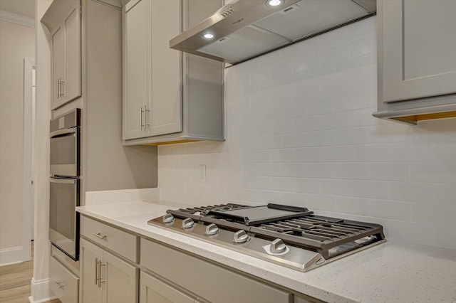 kitchen featuring light stone counters, extractor fan, decorative backsplash, appliances with stainless steel finishes, and light wood-type flooring