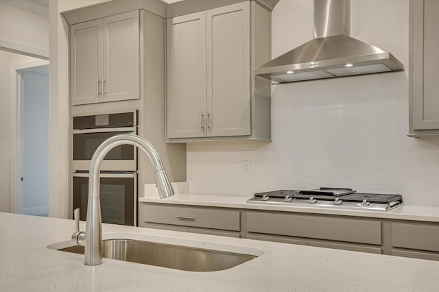 kitchen with gray cabinetry, light stone countertops, wall chimney exhaust hood, and stainless steel appliances