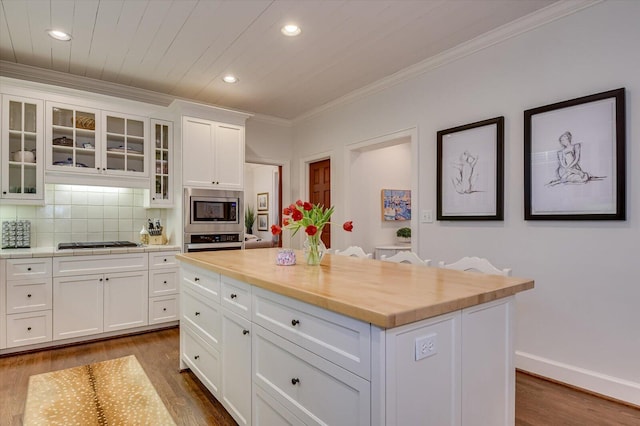 kitchen with dark wood-type flooring, tasteful backsplash, white cabinetry, stainless steel appliances, and crown molding