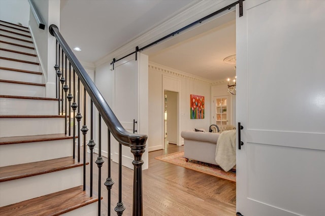 staircase featuring a barn door, wood finished floors, a chandelier, and ornamental molding