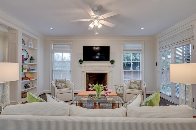 living area featuring built in shelves, a high end fireplace, recessed lighting, crown molding, and ceiling fan