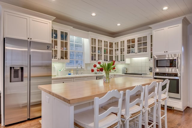 kitchen featuring light wood finished floors, backsplash, ornamental molding, appliances with stainless steel finishes, and white cabinets