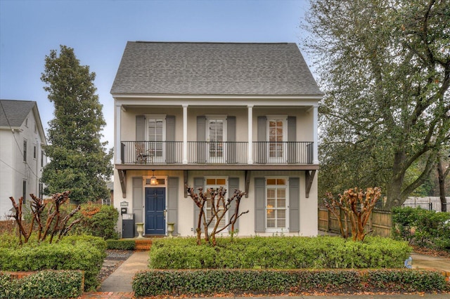 view of front of house featuring a balcony, fence, roof with shingles, and stucco siding