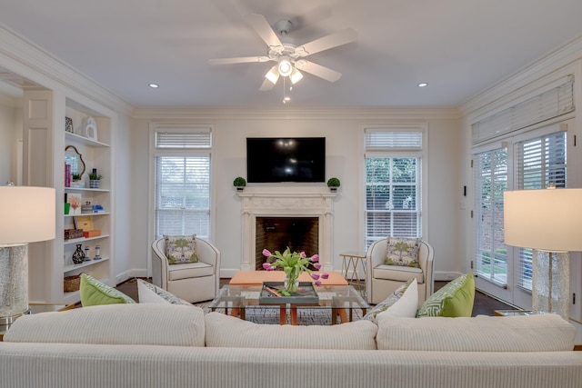 living room with built in features, a fireplace, crown molding, and a ceiling fan