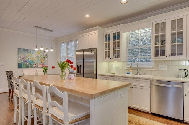 kitchen with a sink, white cabinets, appliances with stainless steel finishes, crown molding, and tasteful backsplash