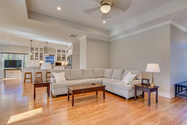 living room featuring a tray ceiling, ceiling fan, and light wood-type flooring