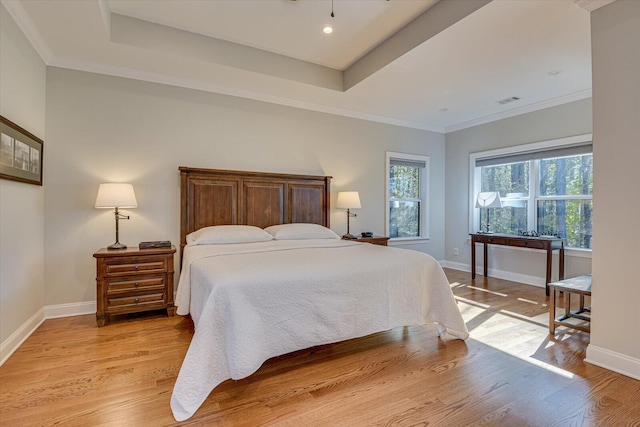 bedroom featuring a tray ceiling, crown molding, and light wood-type flooring