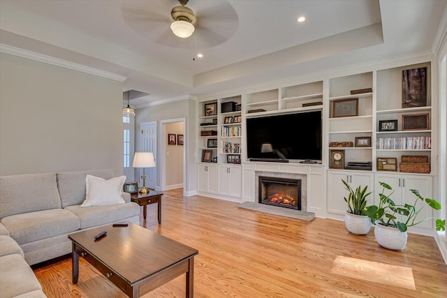 living room with ceiling fan, light hardwood / wood-style floors, built in features, and a tray ceiling