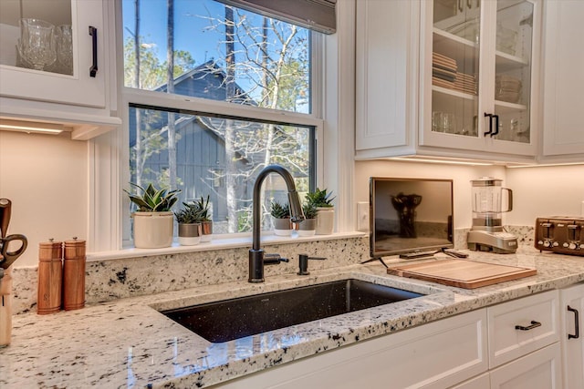 details with white cabinets, light stone counters, and sink