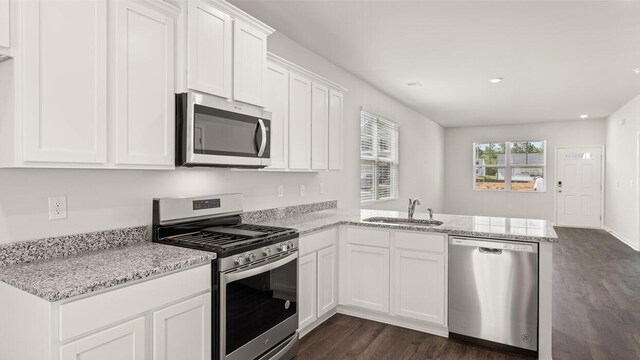kitchen with white cabinetry, a sink, dark wood-style floors, a peninsula, and appliances with stainless steel finishes