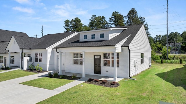 view of front of property featuring a shingled roof, a front yard, a porch, and brick siding
