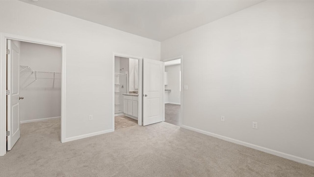 unfurnished bedroom with a closet, baseboards, connected bathroom, light carpet, and a spacious closet