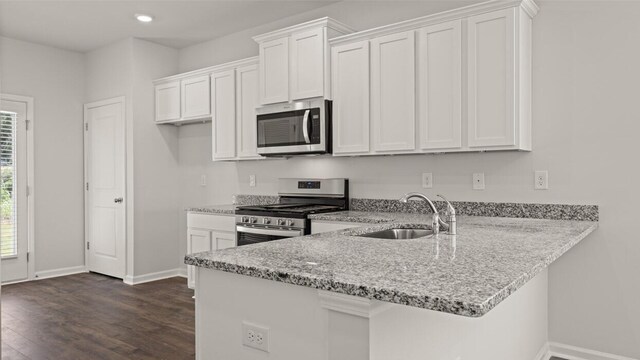 kitchen featuring white cabinets, a peninsula, appliances with stainless steel finishes, a sink, and dark wood-style floors