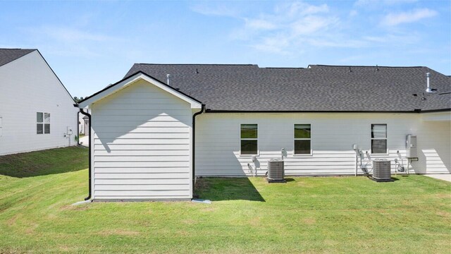 back of property with roof with shingles, central AC, and a yard