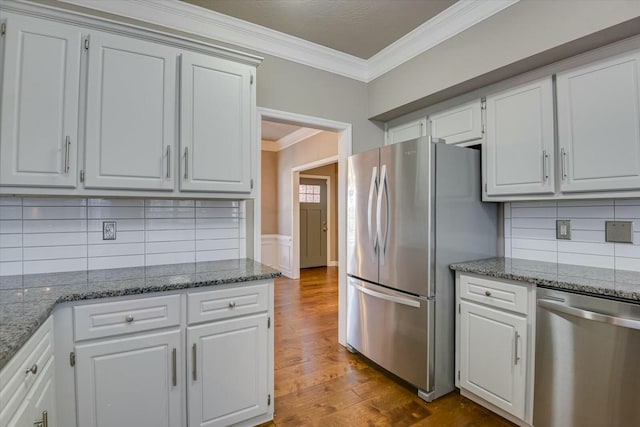 kitchen with white cabinetry, crown molding, wood-type flooring, dark stone countertops, and appliances with stainless steel finishes