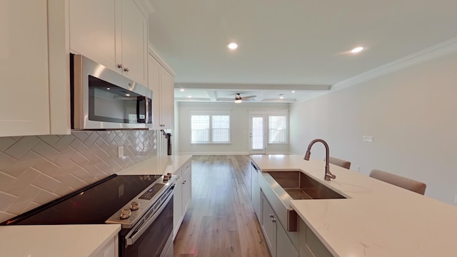 kitchen featuring light stone counters, stainless steel appliances, decorative backsplash, white cabinetry, and a sink