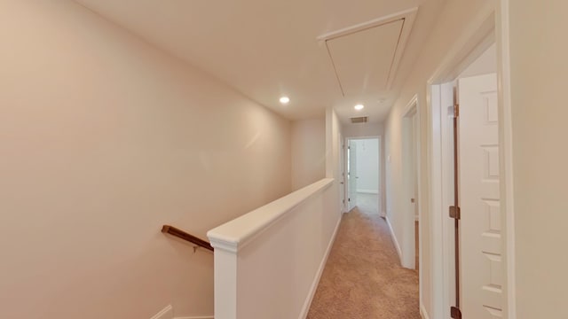 hallway with attic access, baseboards, light colored carpet, and an upstairs landing