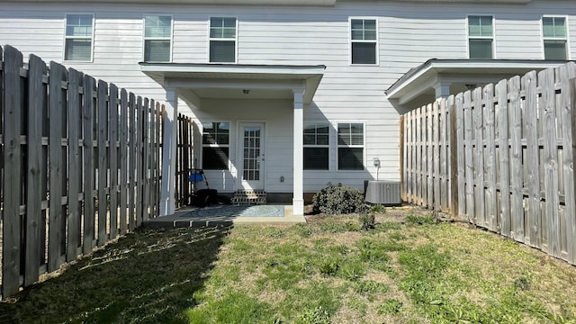 rear view of property with entry steps, a yard, a fenced backyard, and central air condition unit